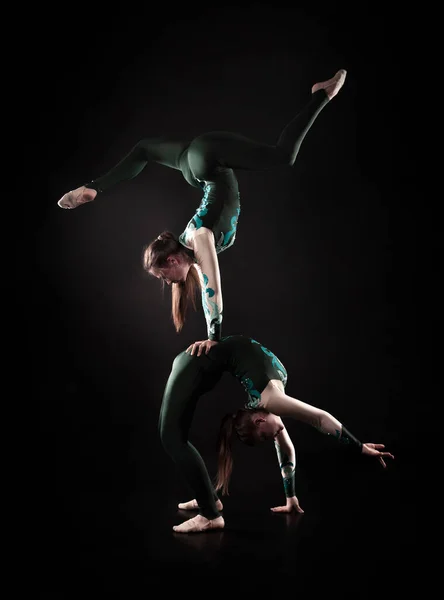 Dos jóvenes equilibradoras femeninas realizan elementos acrobáticos sobre un fondo oscuro con iluminación contorneada . — Foto de Stock