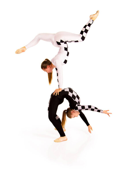 Two young female equilibrists perform acrobatic elements on a white background. Studio shooting.