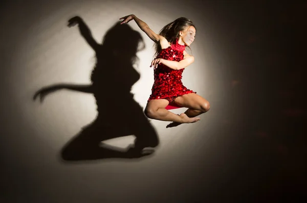 赤いドレスの少女が体操ジャンプをし 白い背景に人物の影が現れる スタジオ撮影 — ストック写真