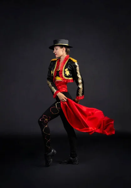 Plastic girl gracefully dancing in a stage costume stylized as a bullfighter. Studio shooting on a dark background.