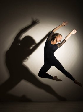 Karanlıkta kız jimnastik atlama gerçekleştirir, beyaz bir arka plan üzerinde bir şekil bir gölge var. Stüdyo fotoğrafçılığı.