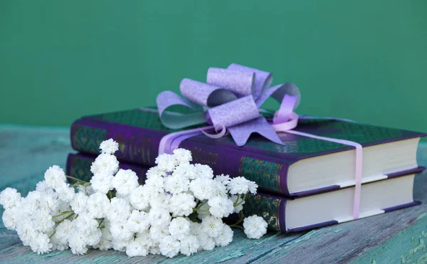 books as a gift on a green background decorated with a bow and a bouquet of white flowers
