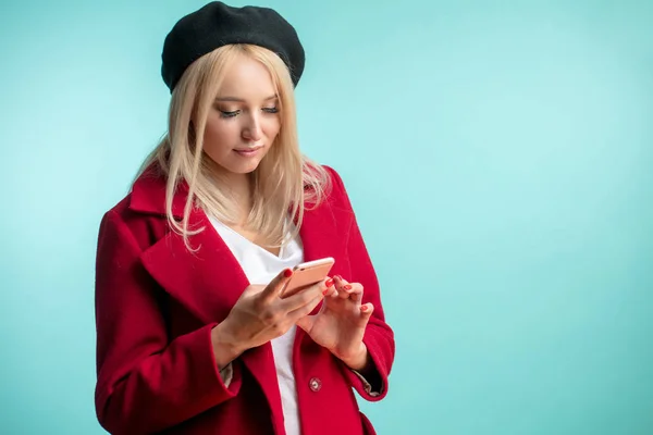 pleasant model in coat and beret looking at the smartphone