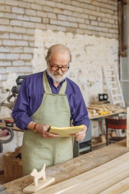 Yaşlı adam mavi gömlek ve önlük giyiyor alıştırma kitabı arıyor