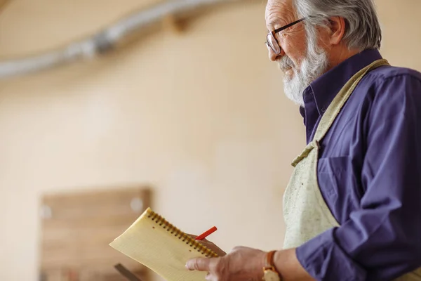 Old worker with moustache nad beard holding notepad — Stock Photo, Image