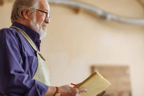 Close-up side view cropped portrait of old carpenter with notepad — Stock Photo, Image