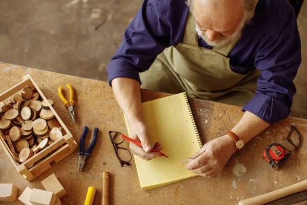 Plano de vista superior del viejo artesano sentado con lápiz y libro de ejercicios —  Fotos de Stock