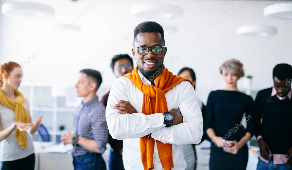 confident handsome black boss with crossed arms in front of co-workers