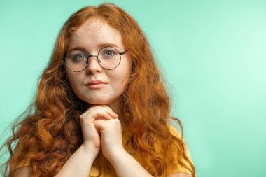 Kızıl saçlı genç bir kadının stüdyoda kameraya baktığı bir fotoğraf.