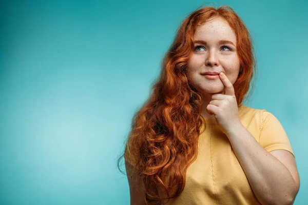 Cute cheerful redhead young girl in yellow over blue background with face. — Stock Photo, Image