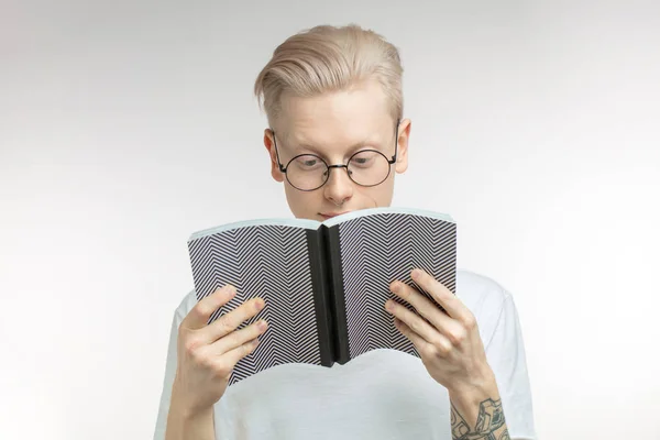 El hombre blanco sonríe y esconde su cara detrás de un libro. Retrato de estudio — Foto de Stock