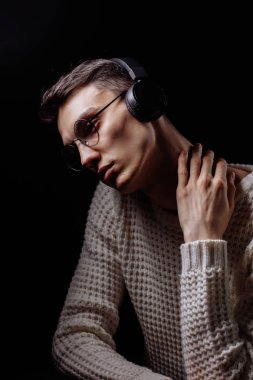 Gözlüklü ve kulaklıklı genç adam siyah arka planda müzik dinliyor.
