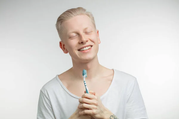 Hombre con los ojos cerrados sosteniendo el cepillo de dientes en la mano. Cuidado dental y salud dental —  Fotos de Stock