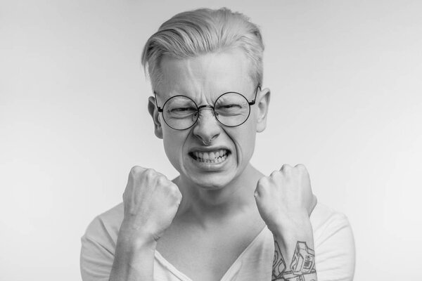 monochrome shot of desparate young student man with squeezing white perfect teeth and clenching fists being extremely upset that he fail important exam.