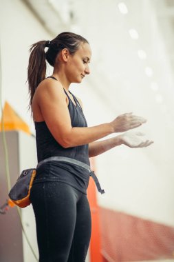Tebeşir gibi elleri olan genç bir kadın kapalı spor salonunun duvarında poz veriyor.