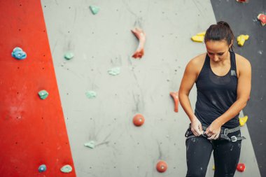 Spor salonunda duvara tırmanan bir kadının koşum takımını çalıştıran antrenör.