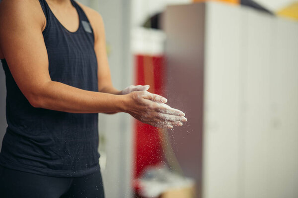 young woman with chalked hands posing at indoor climbing gym wall