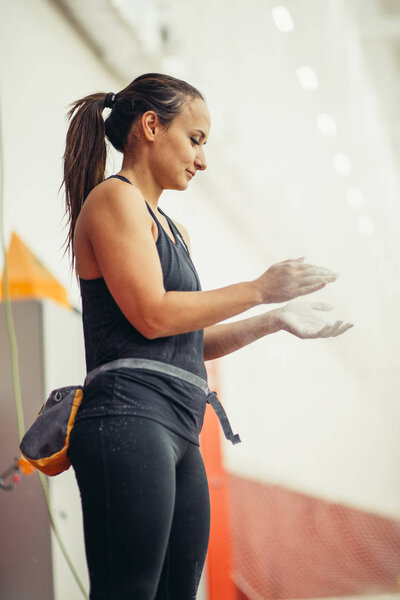 young woman with chalked hands posing at indoor climbing gym wall