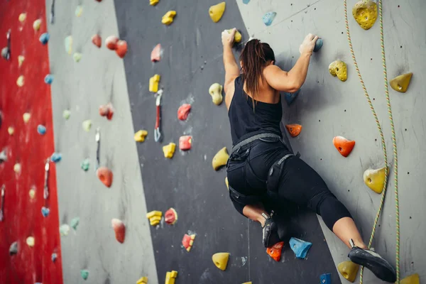 Sportliche junge Frau trainiert in einer bunten Kletterhalle. — Stockfoto