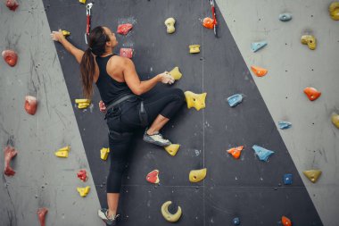 Genç dağcı kadın tırmanış merkezinde pratik kayalara tırmanıyor, kaya tırmanıyor.