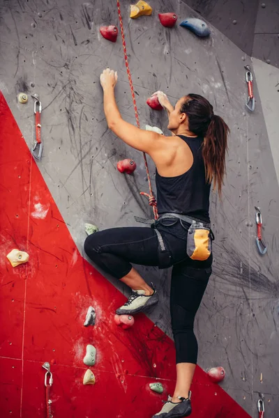 Młoda kobieta robi profesjonalne głazy w siłowni wspinaczkowej w pomieszczeniach — Zdjęcie stockowe