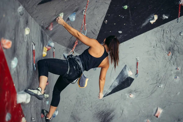 Femeia ajunge în partea de sus a peretelui artificial de bolovani în timp ce exercită în sala de sport . — Fotografie, imagine de stoc