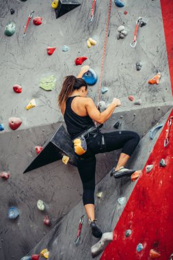 Renkli bir tırmanma salonunda spor yapan genç bir kadın. Serbest dağcı kız içeri tırmanıyor.