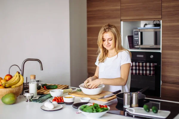 Porträtt av lycklig kvinnlig fru i vit t-shirt matlagning middag i köket — Stockfoto