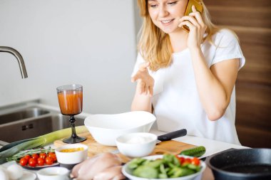 Beyaz kadın sağlıklı yemek yapıyor ve telefondaki mesajları okuyor..