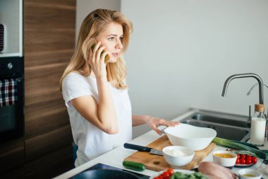Beyaz kadın sağlıklı yemek yapıyor ve telefondaki mesajları okuyor..
