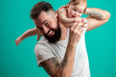 Oynak babası onun gülümseyen bebek çocuk boynuna mavi arka plan üzerinde taşıyor.