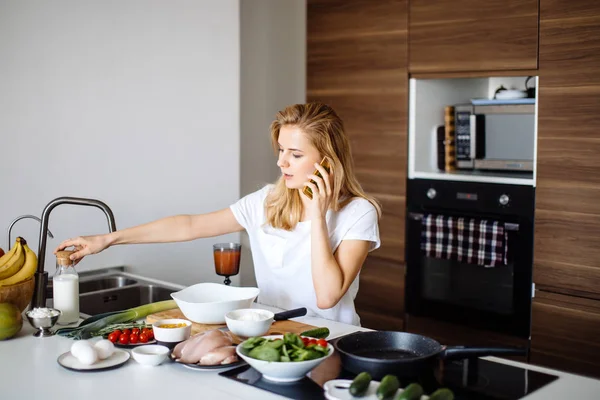 Caucasian woman making healthy meal and reading message at phone in kitchen. — Stock Photo, Image