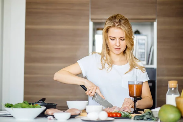 Woman cutting chiken meat on a kitchen table with a big Chef knife — Stock Photo, Image