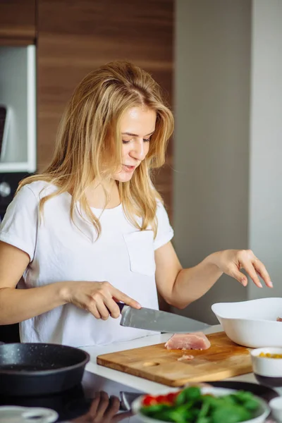 Woman cutting chiken meat on a kitchen table with a big Chef knife — Stock Photo, Image