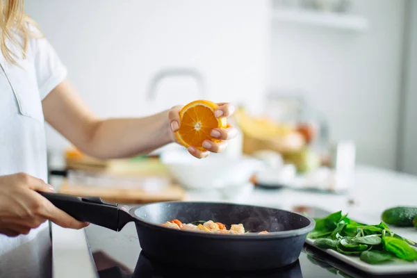 Joven ama de casa cocinando en la cocina, exprimiendo la naranja en la sartén — Foto de Stock