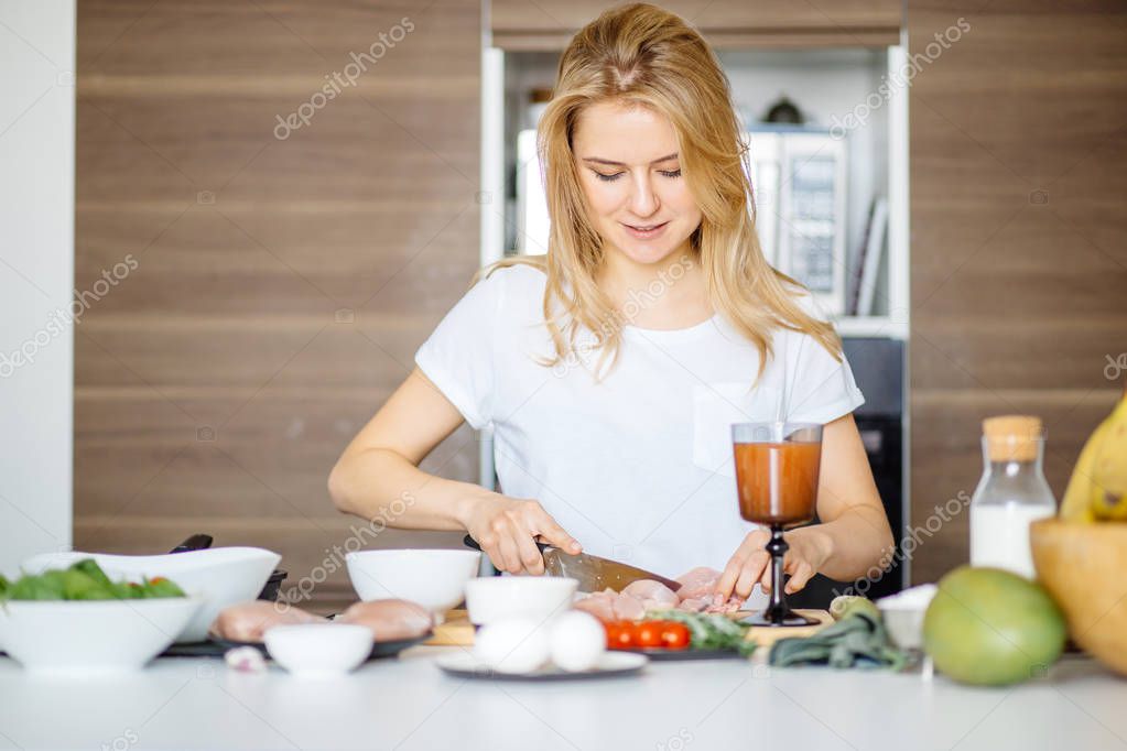 Woman cutting chiken meat on a kitchen table with a big Chef knife