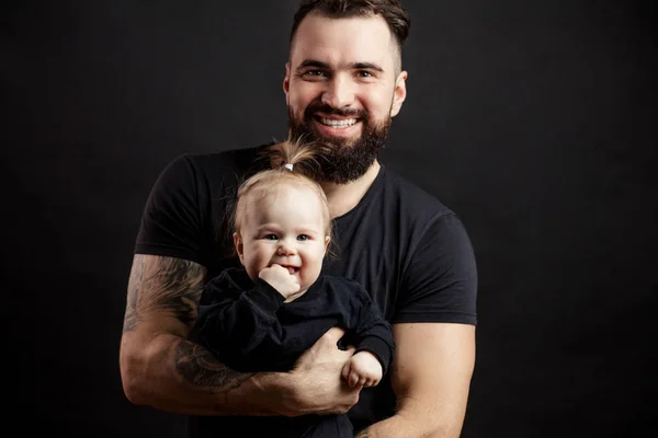 Jovem pai atlético com bebê adorável no fundo preto — Fotografia de Stock