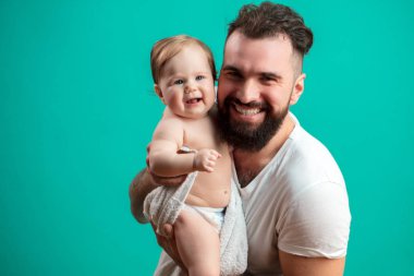 Onun gülümseyen bebek çocuk boynunda taşıyan ve onunla stüdyoda mavi arka plan üzerinde oynarken oynak babası