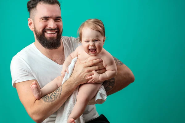 Pai brincalhão carregando seu filho bebê sorridente no pescoço sobre fundo azul — Fotografia de Stock