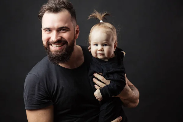 Jovem pai atlético com bebê adorável no fundo preto — Fotografia de Stock