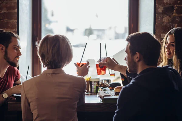 Vista posteriore della compagnia di giovani felici che parlano mentre sono seduti al caffè — Foto Stock