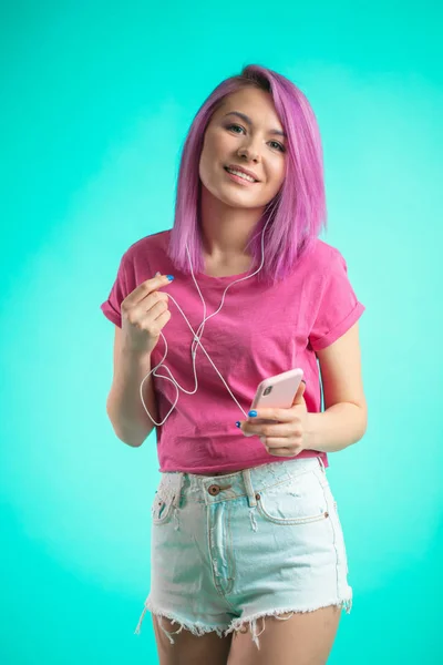 Wanita berambut merah muda mendengarkan musik di headphone di latar belakang biru . — Stok Foto