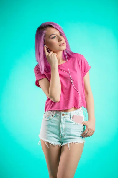Rózsaszín hajú hölgy zenehallgatás fejhallgató a kék háttér. — Stock Fotó