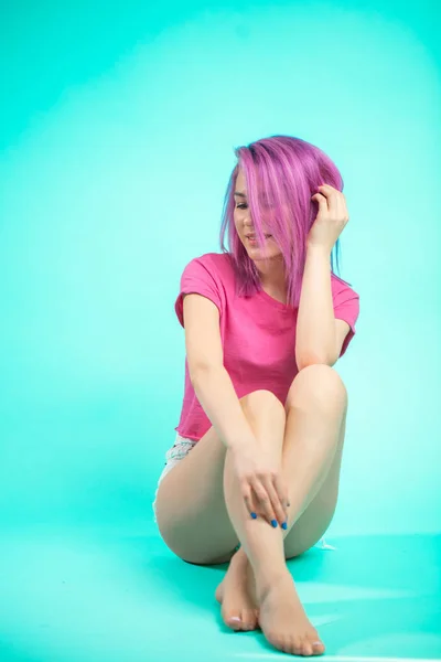笑みを浮かべて ブルー スタジオの床の上に座ってカメラ目線のピンク色の髪を持つ明るい美しい少女の肖像画 — ストック写真