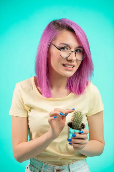 Mulher bonita com cabelo violeta segurando cacto em panela e tocando espinhos — Fotografia de Stock