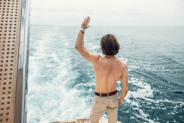 Rückansicht eines jungen Mannes, der am Rand der Jacht sitzt und aufs Meer blickt — Stockfoto