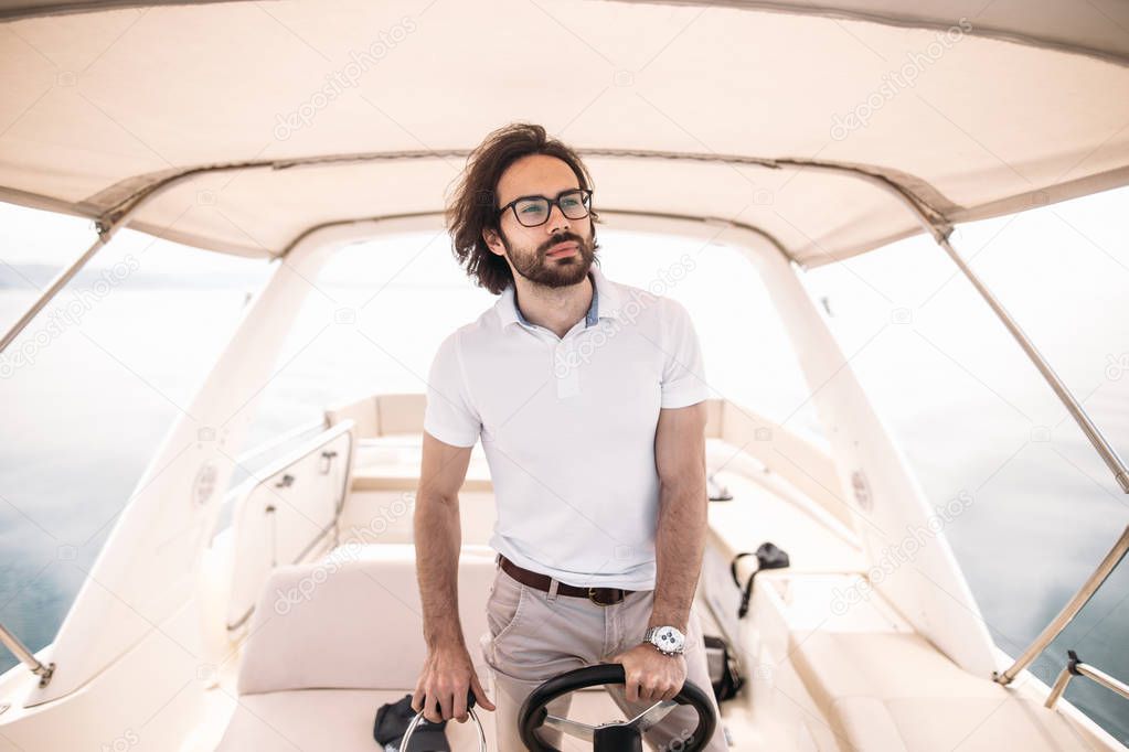 Young handsome bearded sailor man driving his motor boat