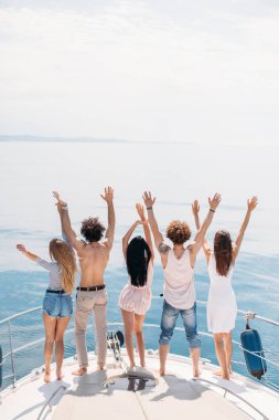 Okyanustaki yelkenlide kutlama yapan arkadaşların arka görüntüsü, kollar havada..