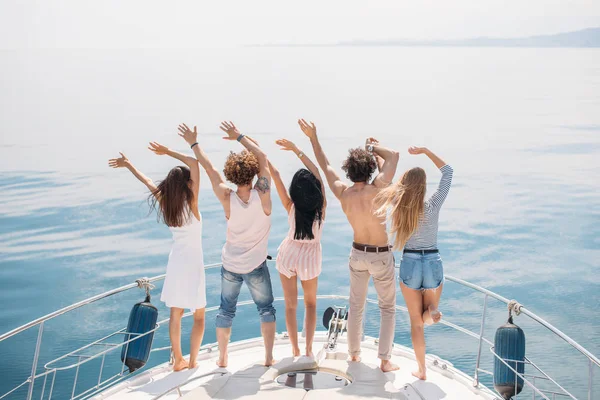 Rear view of friends celebrate on sailboat in ocean, arms raised. — Stock Photo, Image