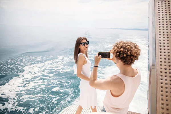 Young photographer taking picture of his girlfriend on seaboat — Stock Photo, Image